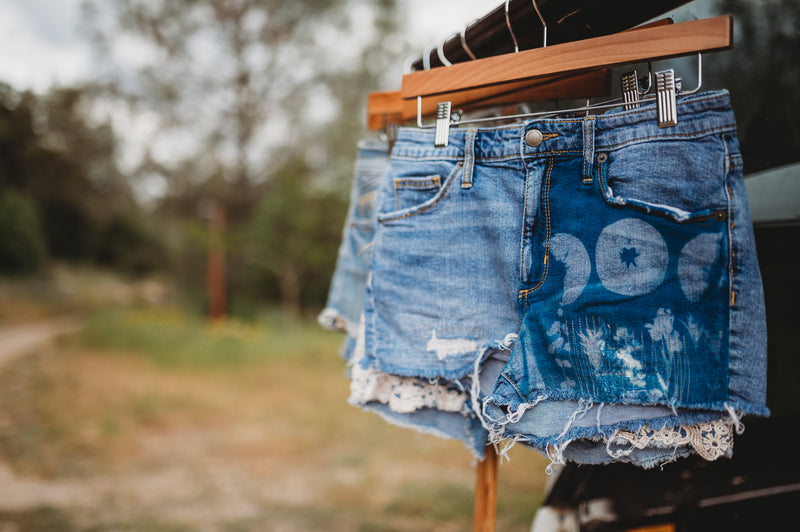 Pair of denim shorts on a hanger with a blurred natural background