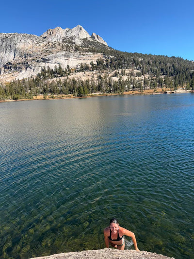 Person sitting on a rock by a lake with mountains in the background
