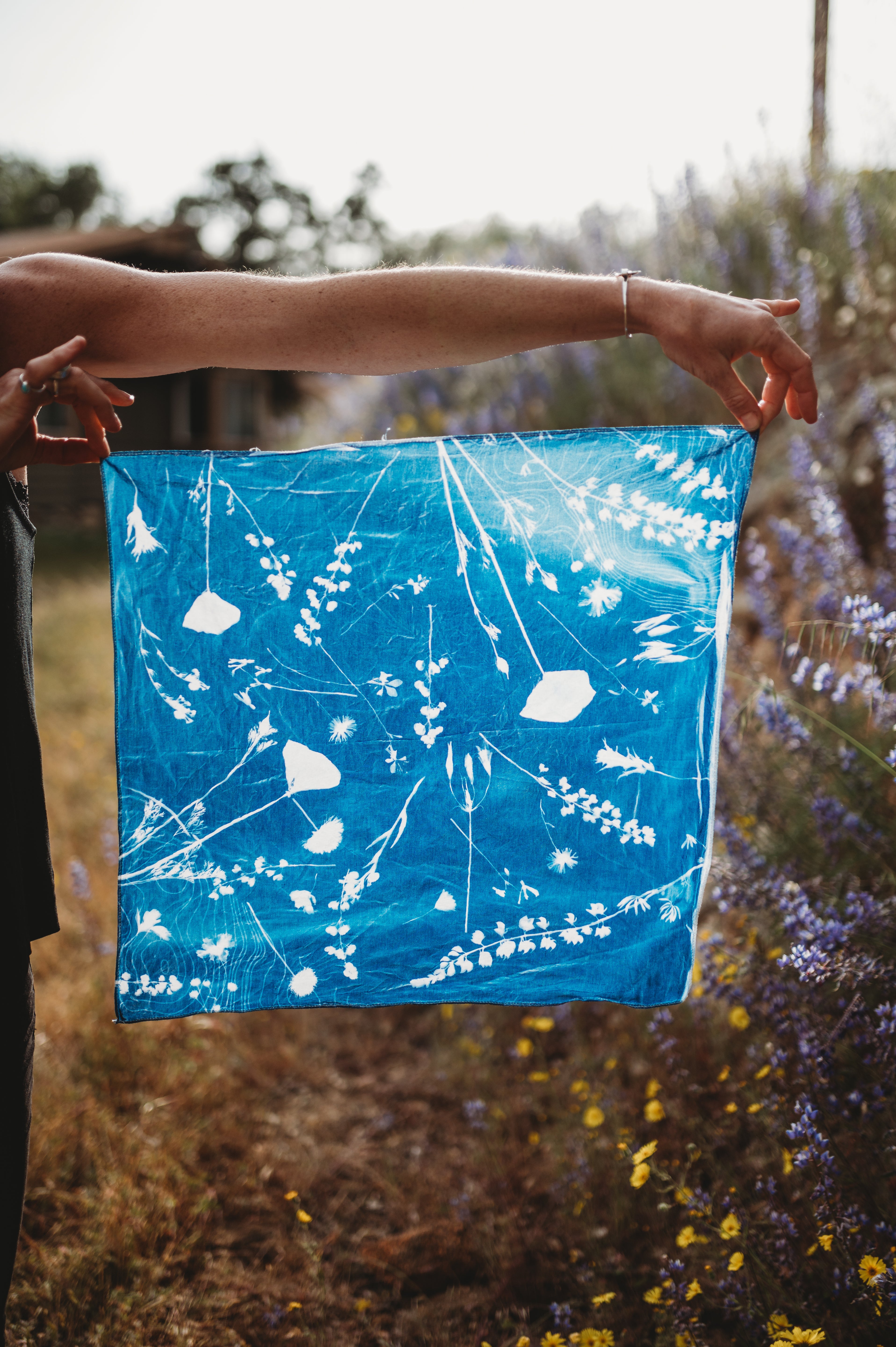 Person holding a blue fabric with white floral patterns against a natural background