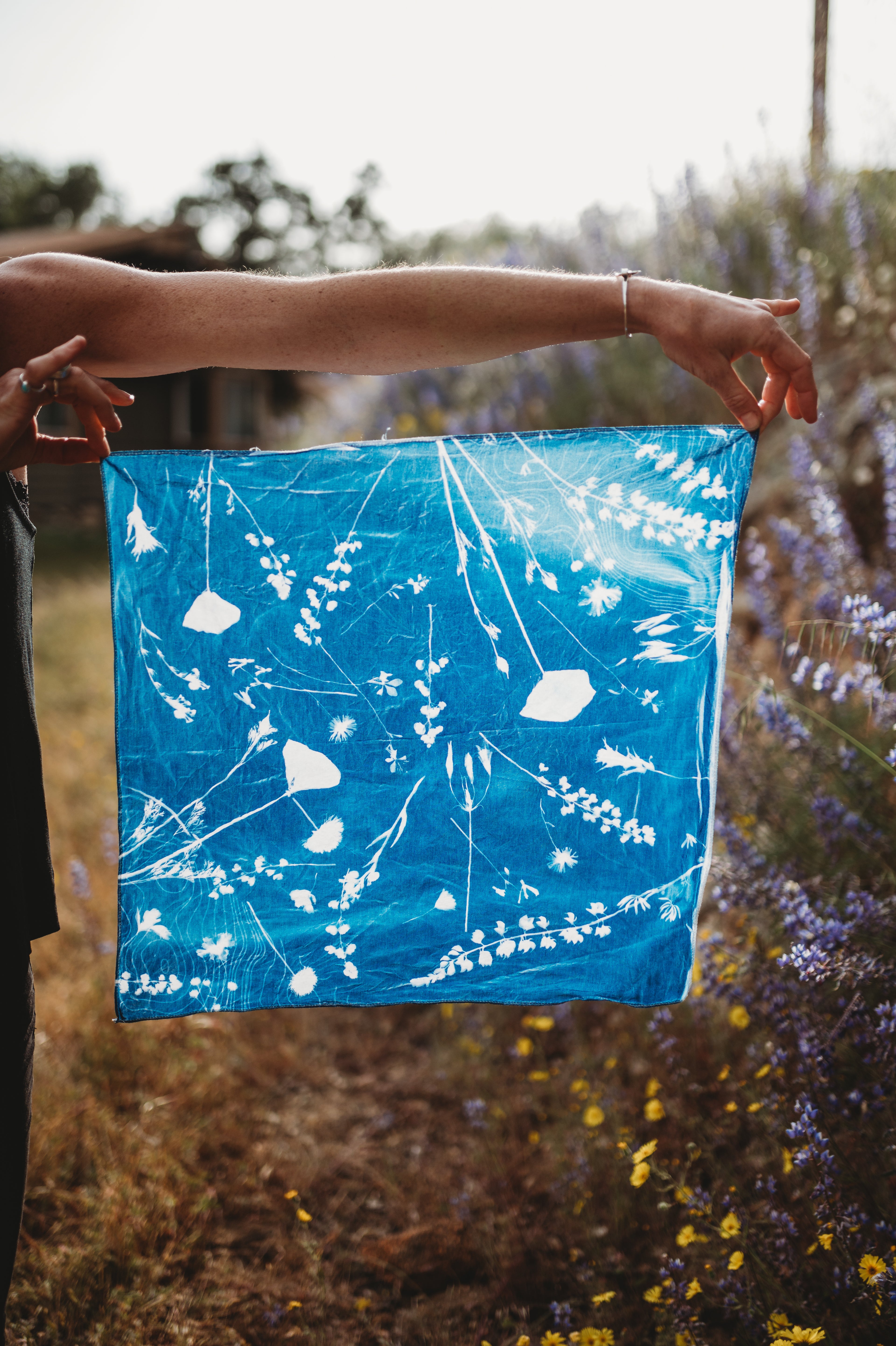 Person holding a blue fabric with white floral patterns against a natural background